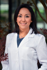 A woman in white lab coat standing next to trees.