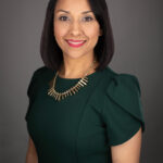 A woman in green dress with necklace and black hair.